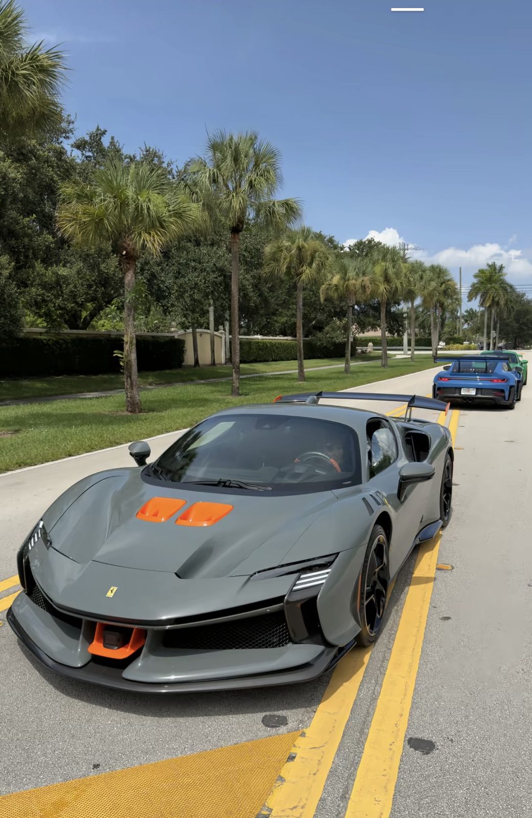 Grey Ferrari SF90 XX with orange accents leading a line of Porsche GT3 RS cars after an exotic vehicle detail