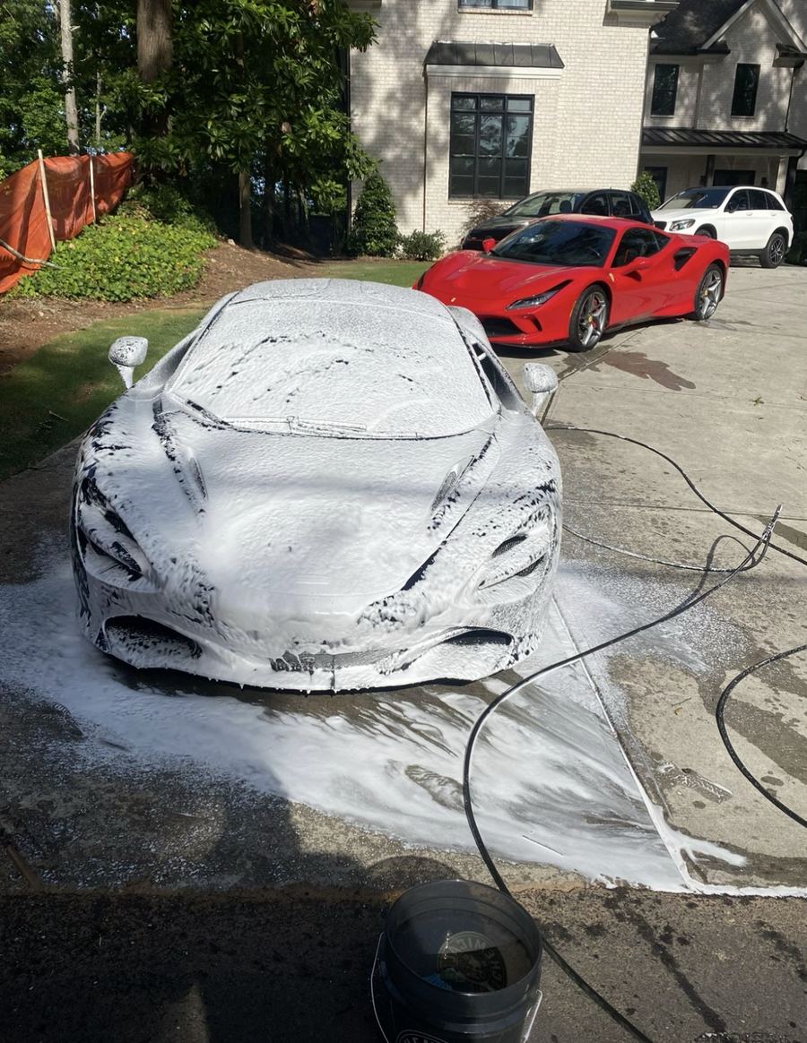 McLaren 720S covered in snow foam during a mobile hand wash on a client driveway, red Ferrari F8 parked behind it